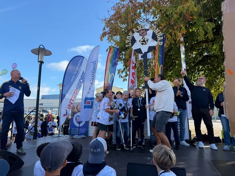 Award ceremony on stage with athletes and officials holding trophy under blue sky and promotional banners