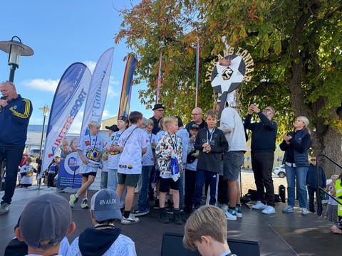 Group of runners and officials at an outdoor race event with blue banners and autumn trees in background