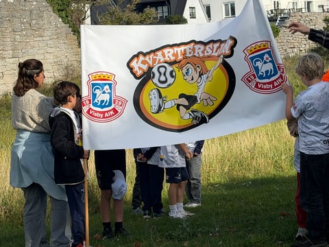 Group of children and adults holding a Scouting banner outdoors on grass