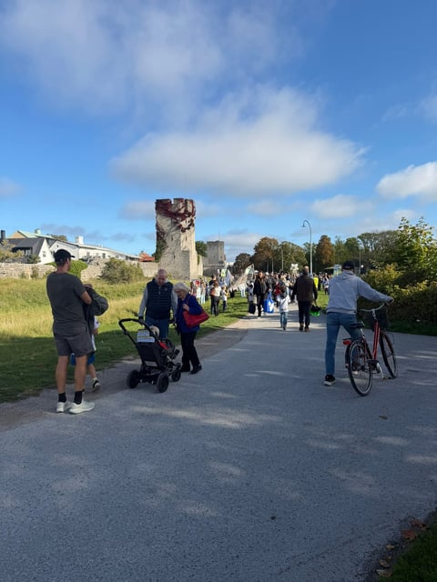 Visitors walking and cycling on a path toward historic stone ruins under a blue sky with clouds