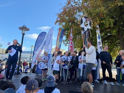 Outdoor water sports event with athletes on stage, spectators watching, promotional banners and surfboards displayed