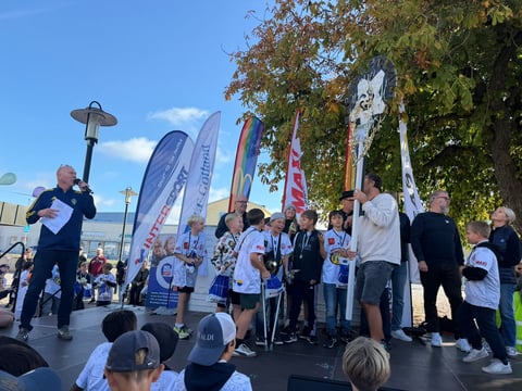 Group of people gathered at outdoor event with banners and flags on stage under blue sky