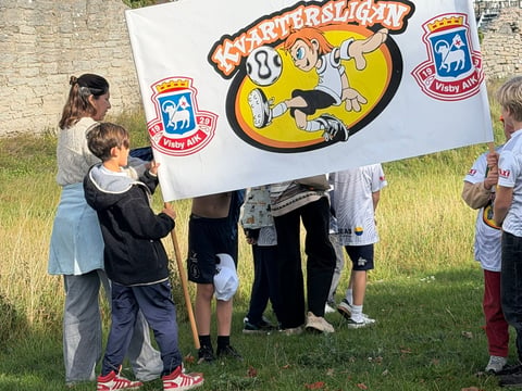 Children holding a large Underdog cartoon banner outdoors at what appears to be a community event or gathering on grass