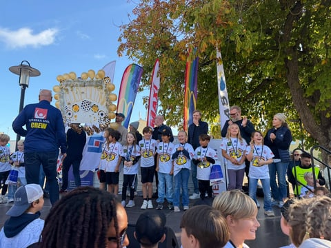 Group of young athletes and children on a stage at an outdoor event with colorful banners and spectators